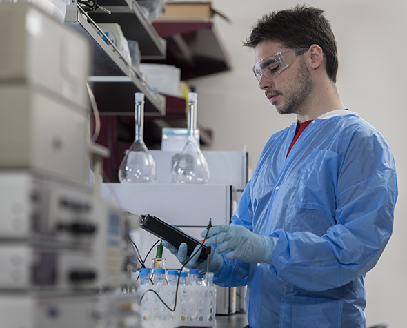 A student in a lab gown in a lab with vials on the table
